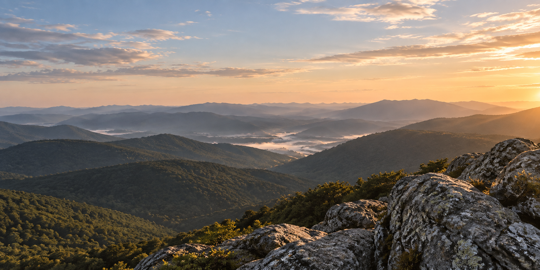 Rocky mountain summit overlooking layered ridgelines beneath a warm dawn sky